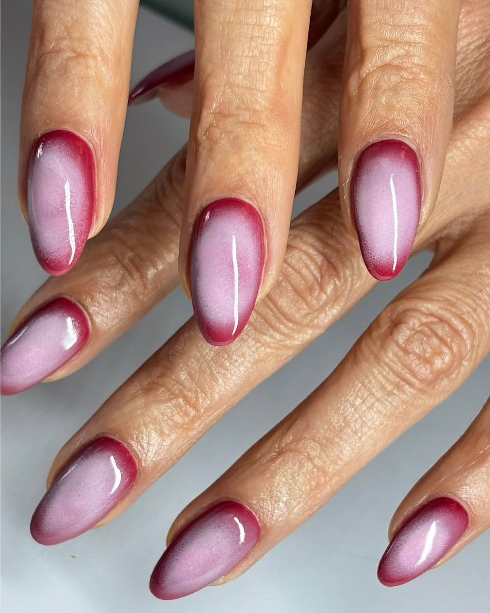 Glossy almondshaped nails with light pink blooming from crimson border.