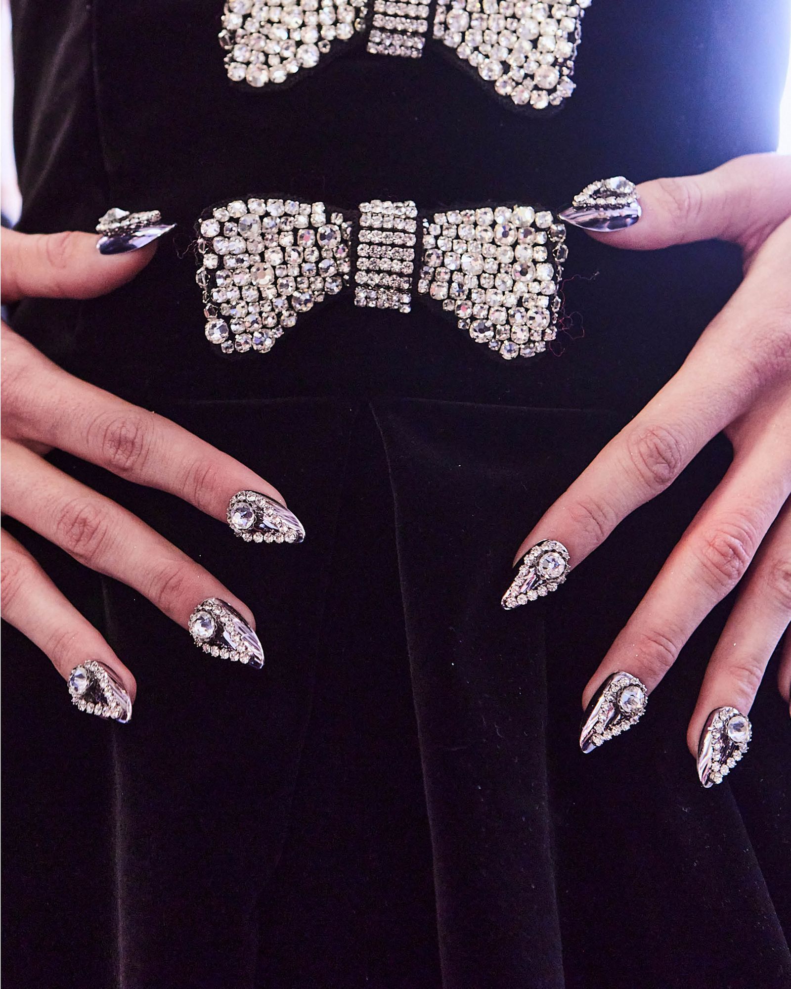 3D chromatic gem nails displayed on a black dress with gemencrusted bows.