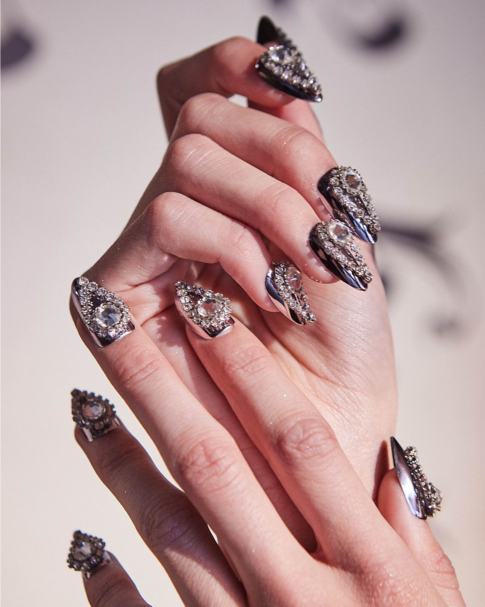 Folded fingers showing chromatic 3D gem nail designs in tear drop shape.