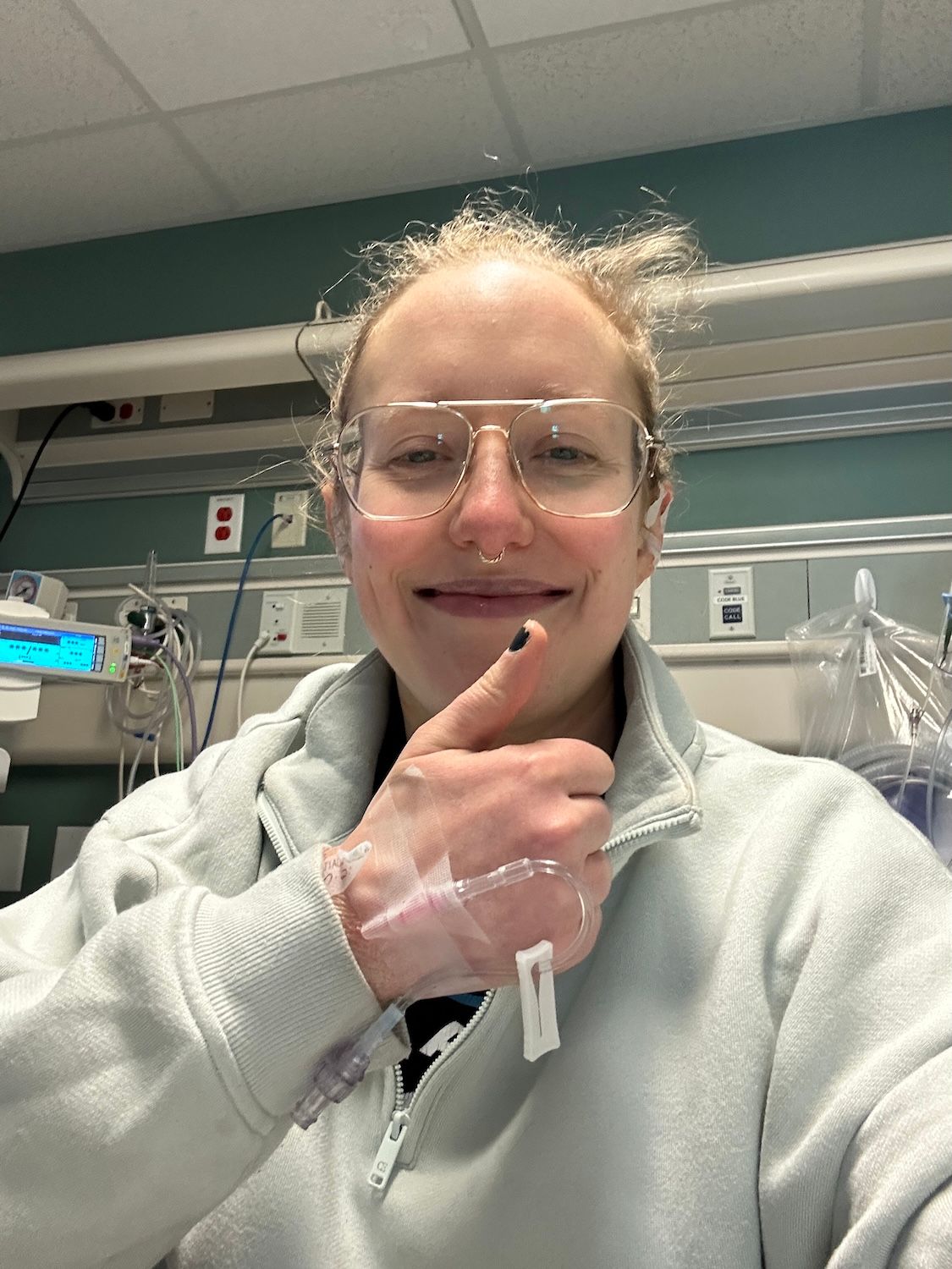woman immediately after breast surgery giving thumbs up with IV in hand