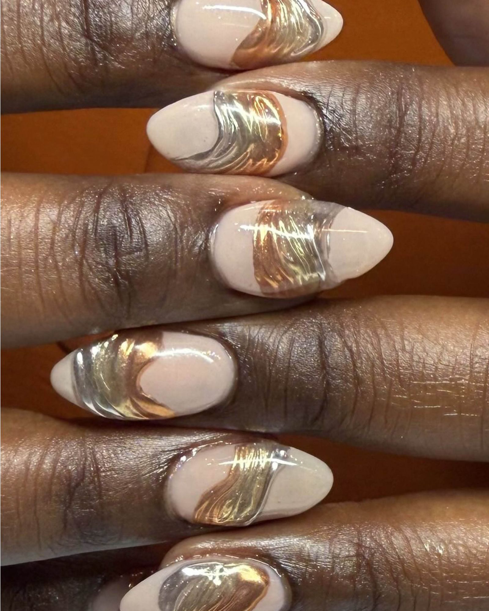 Interlocked fingers showing nude almond shaped nails with wavy metallic middle section that flows from gold to silver.