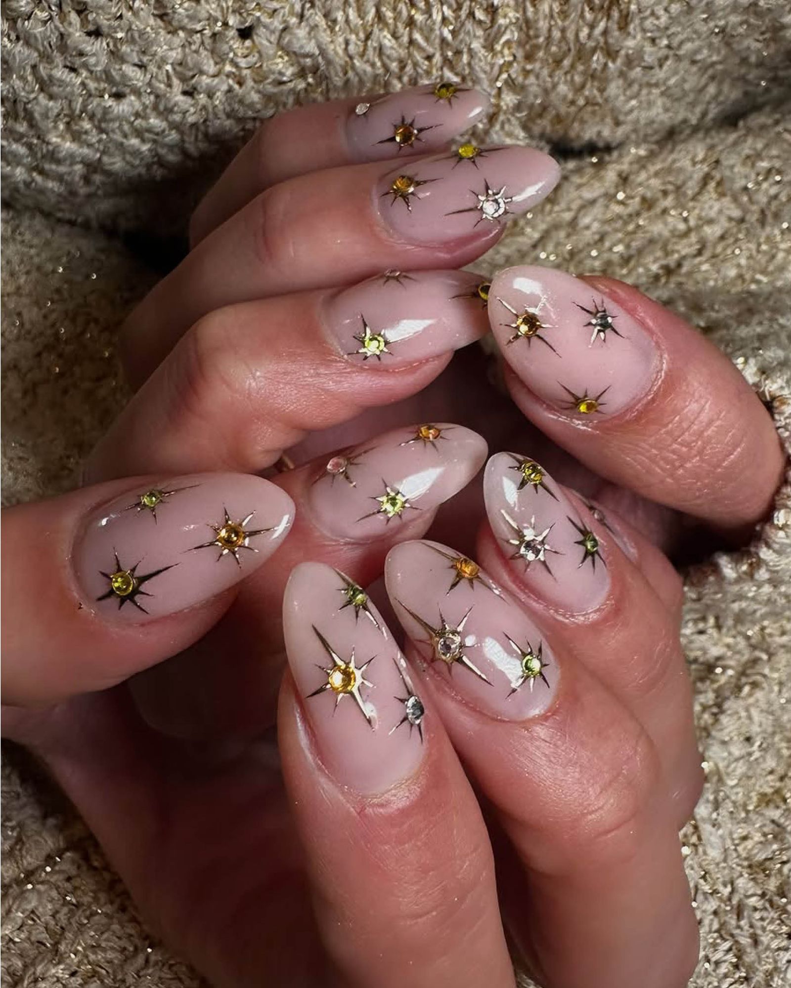 Nude glossy nails with gold and silver twinkling star designs and gems.