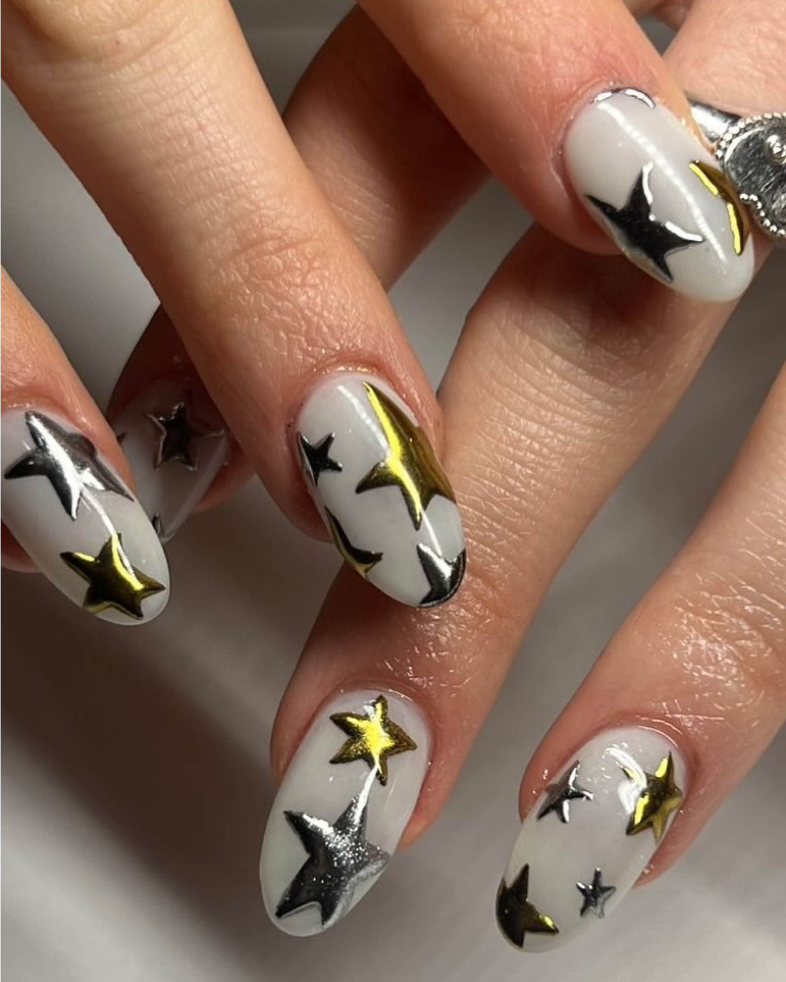 Fingers layered to show cool white base nails with large gold and silver star designs.