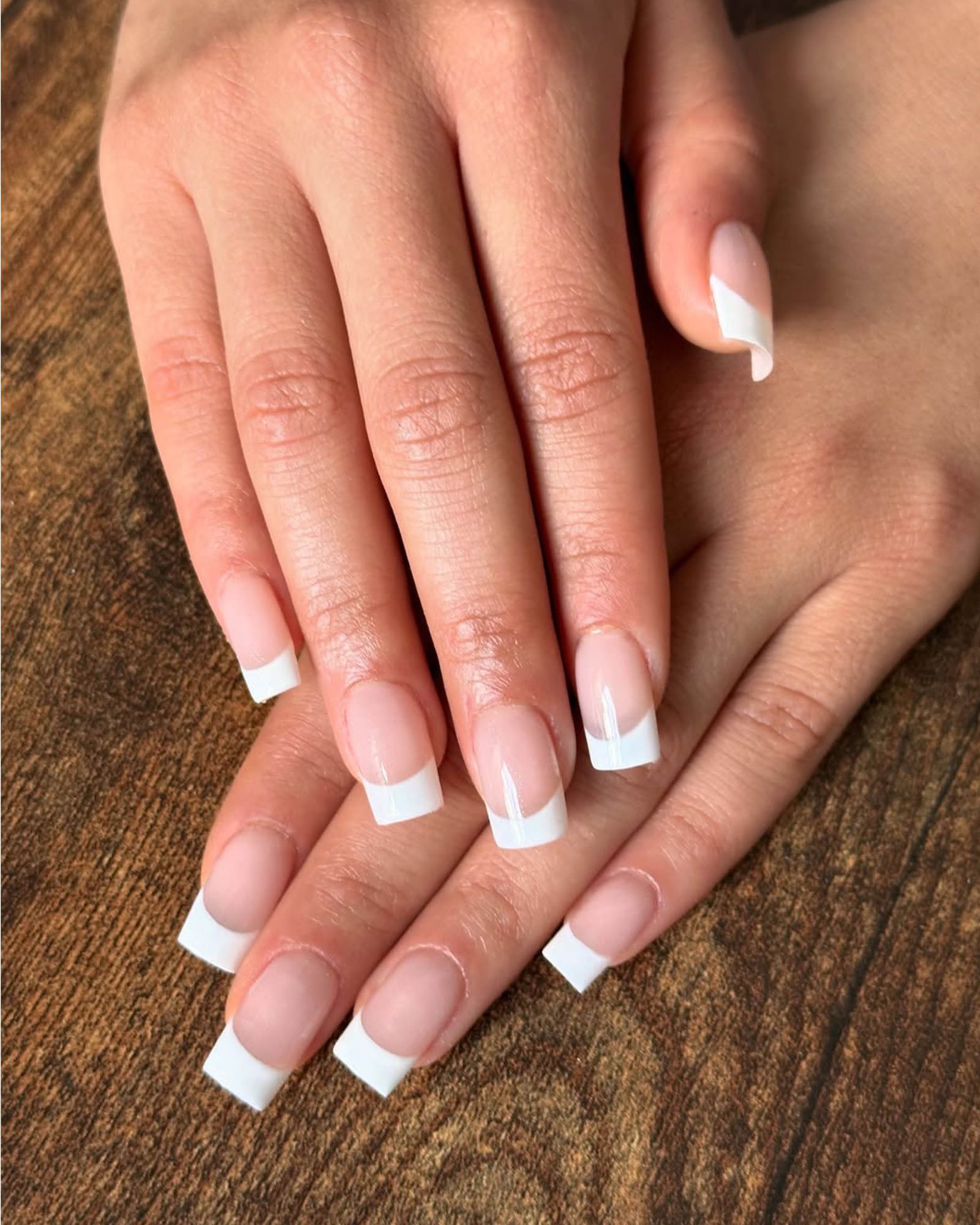 One hand layered flat on the other showing classic square cut French tip manicure.