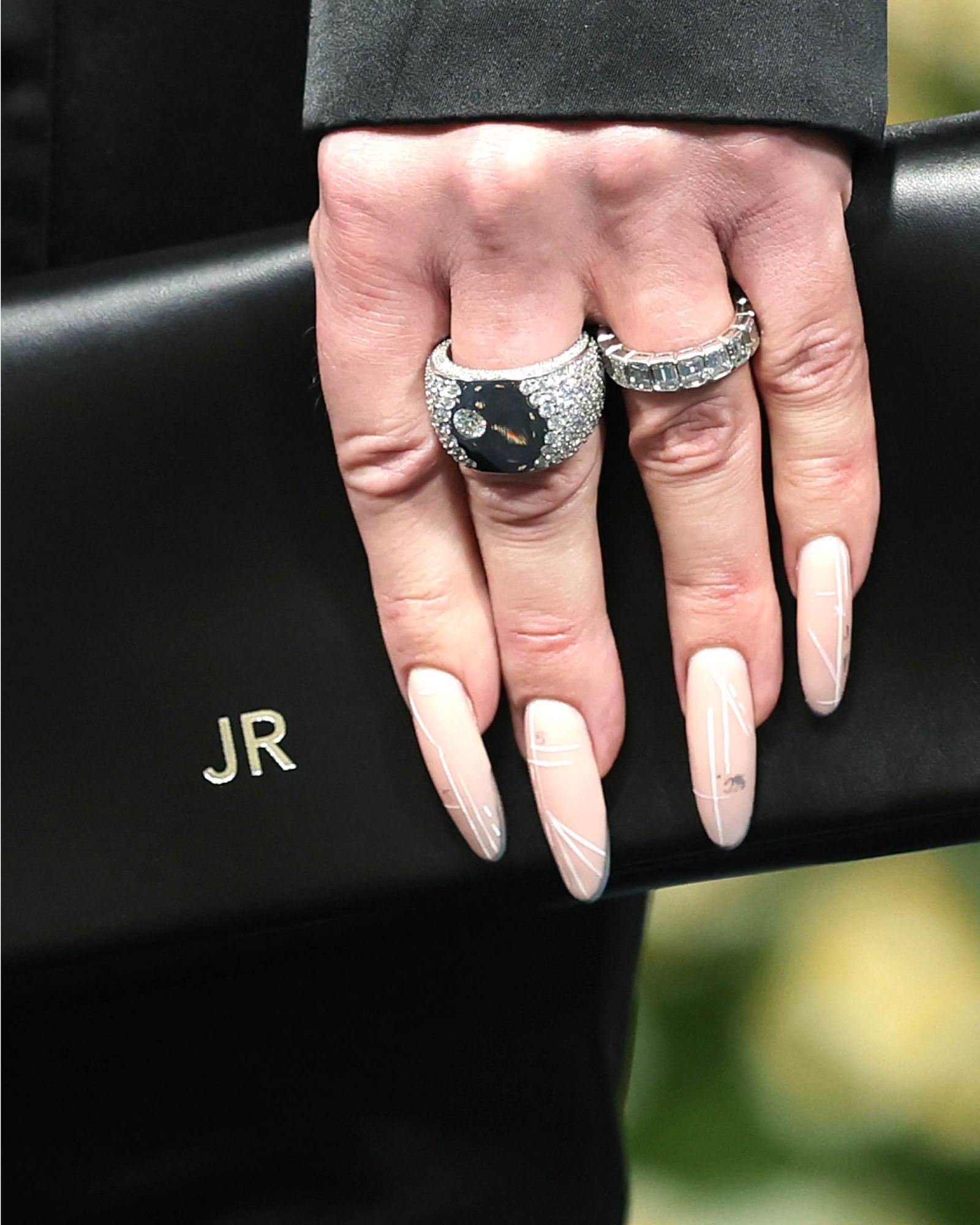 Hand holding a clutch monogrammed with JR showcases long nude nails with thin white stripes in abstract design.