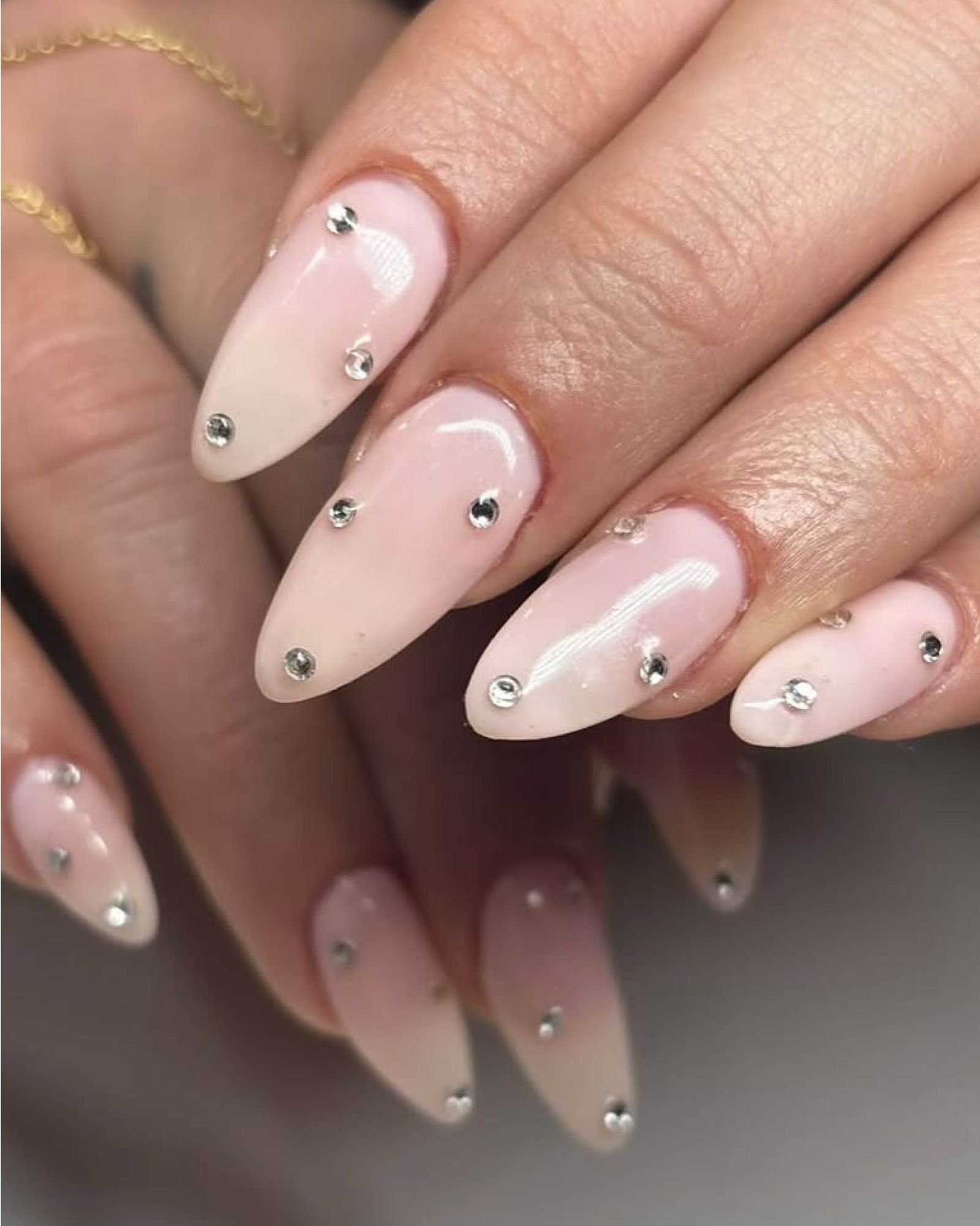 One hand layered on the other to show almondshaped acrylic pinky nude nails with interspersed silver gems.