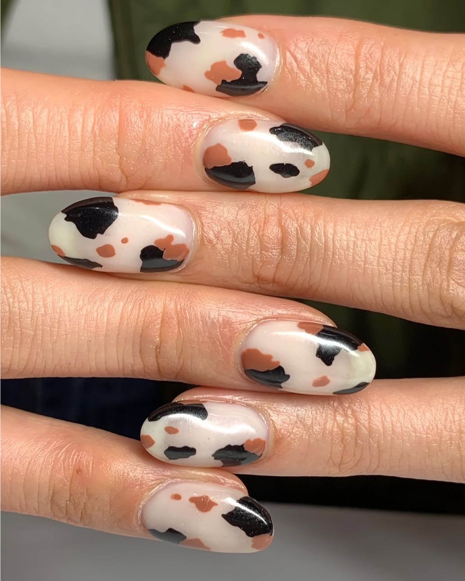 Interlocked fingers feature cream nail base with brown and black cow hide spots.