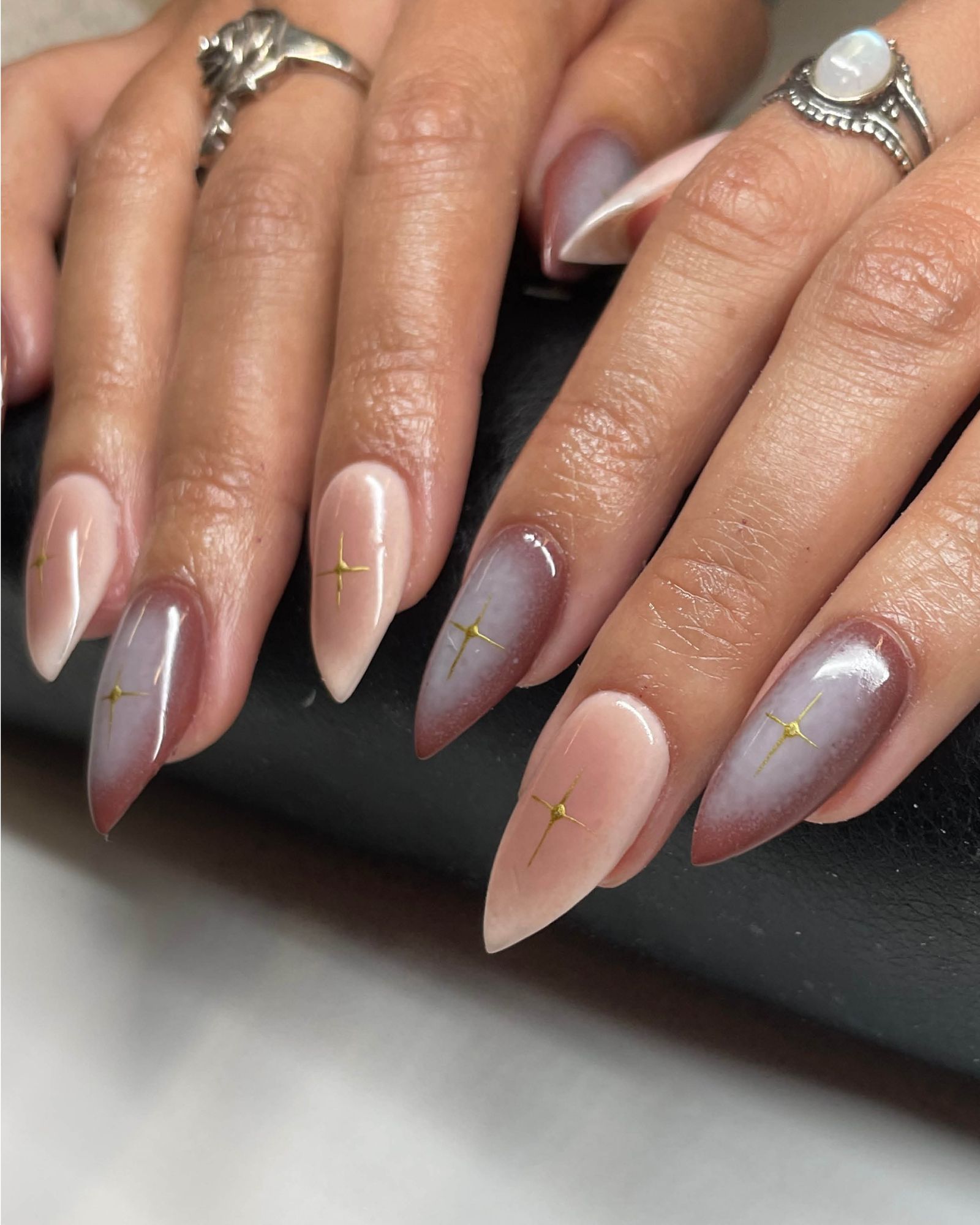 Neutral nude brown and mauve soft aura nails with gold sparkle icons in the center of the nail.