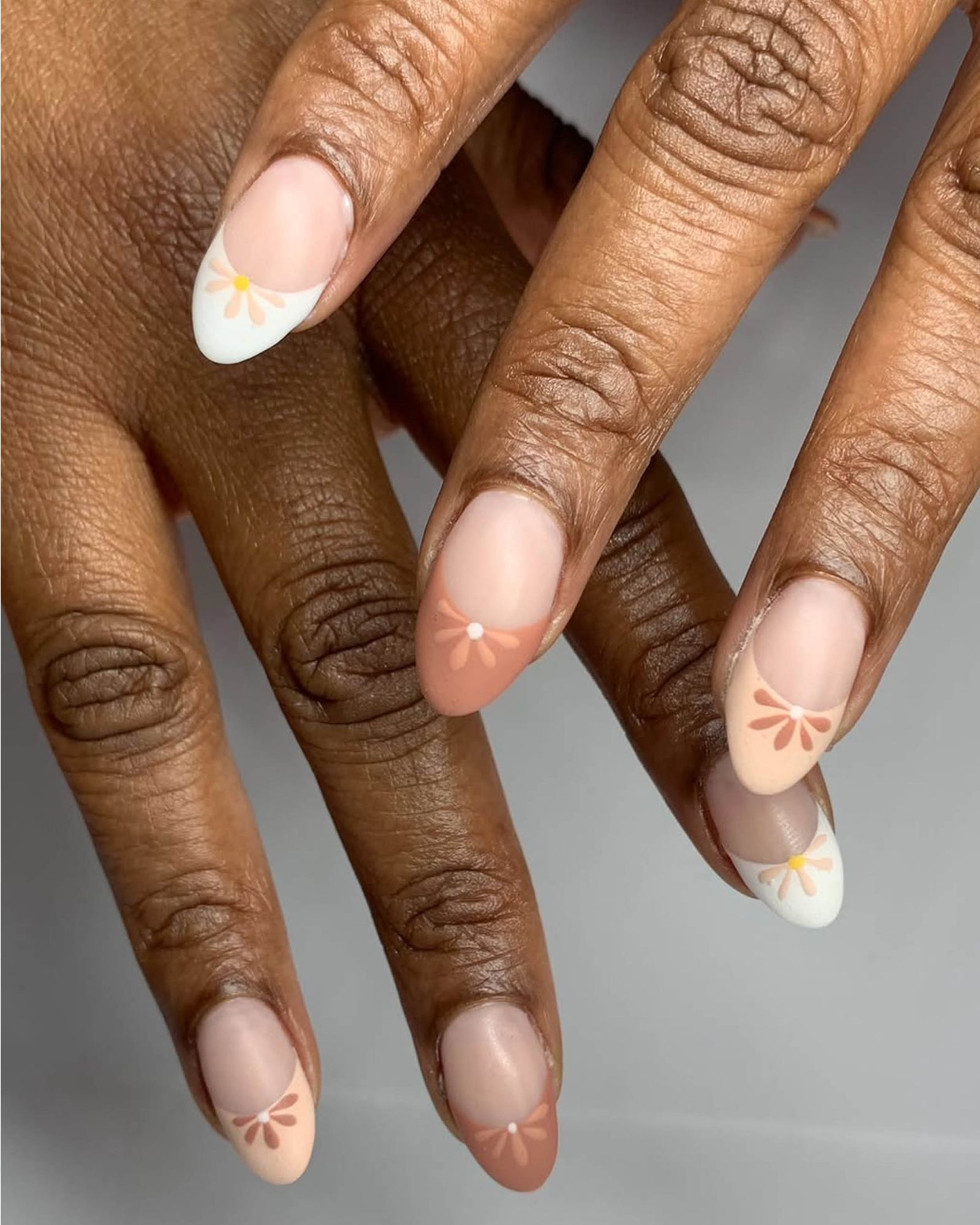 Matte nude nails with multicolored neutral French tips and half daisies.