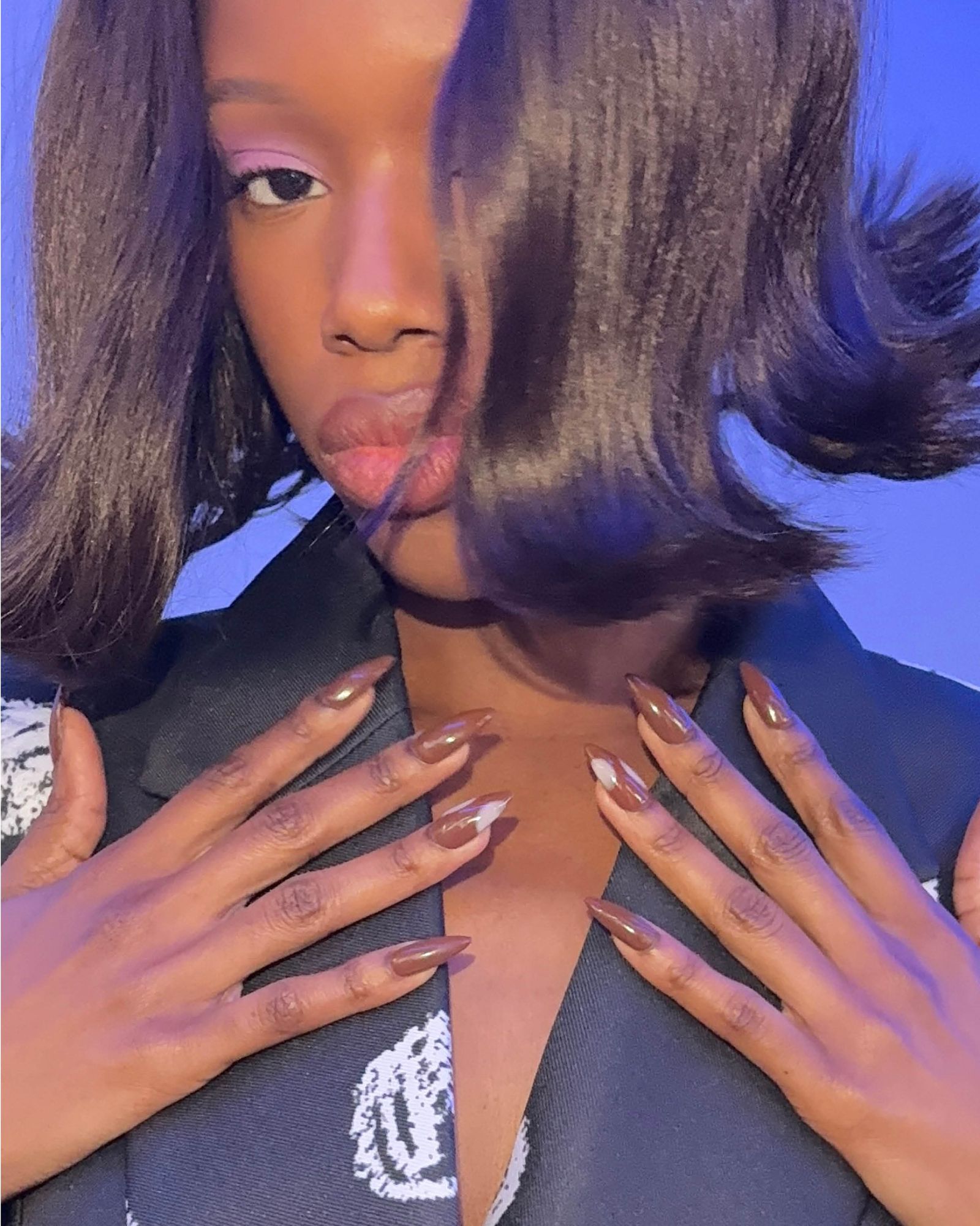 Long neutral nails with a few polka dots displayed at the collar of a jacket.