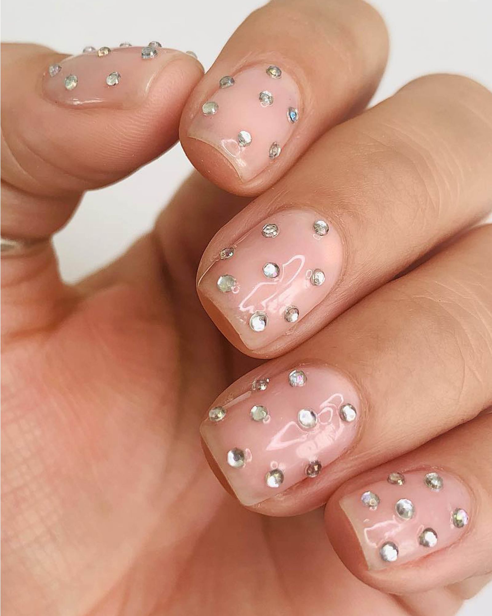 Fingers on one hand curled upwards to show silver gems in polka dot fashion on nude nail base.