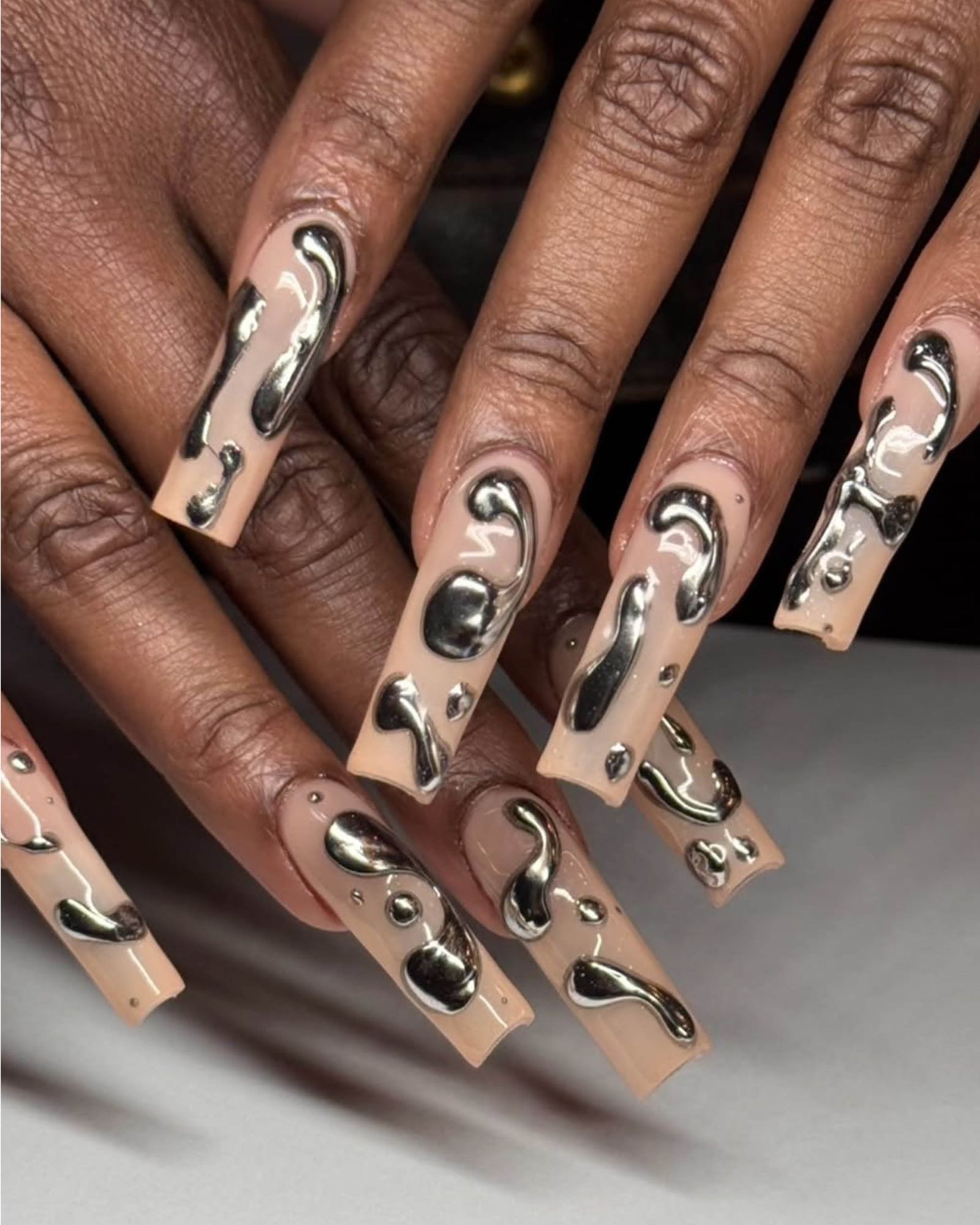Silver chrome drip on long acrylic squareshaped nails with nude base.