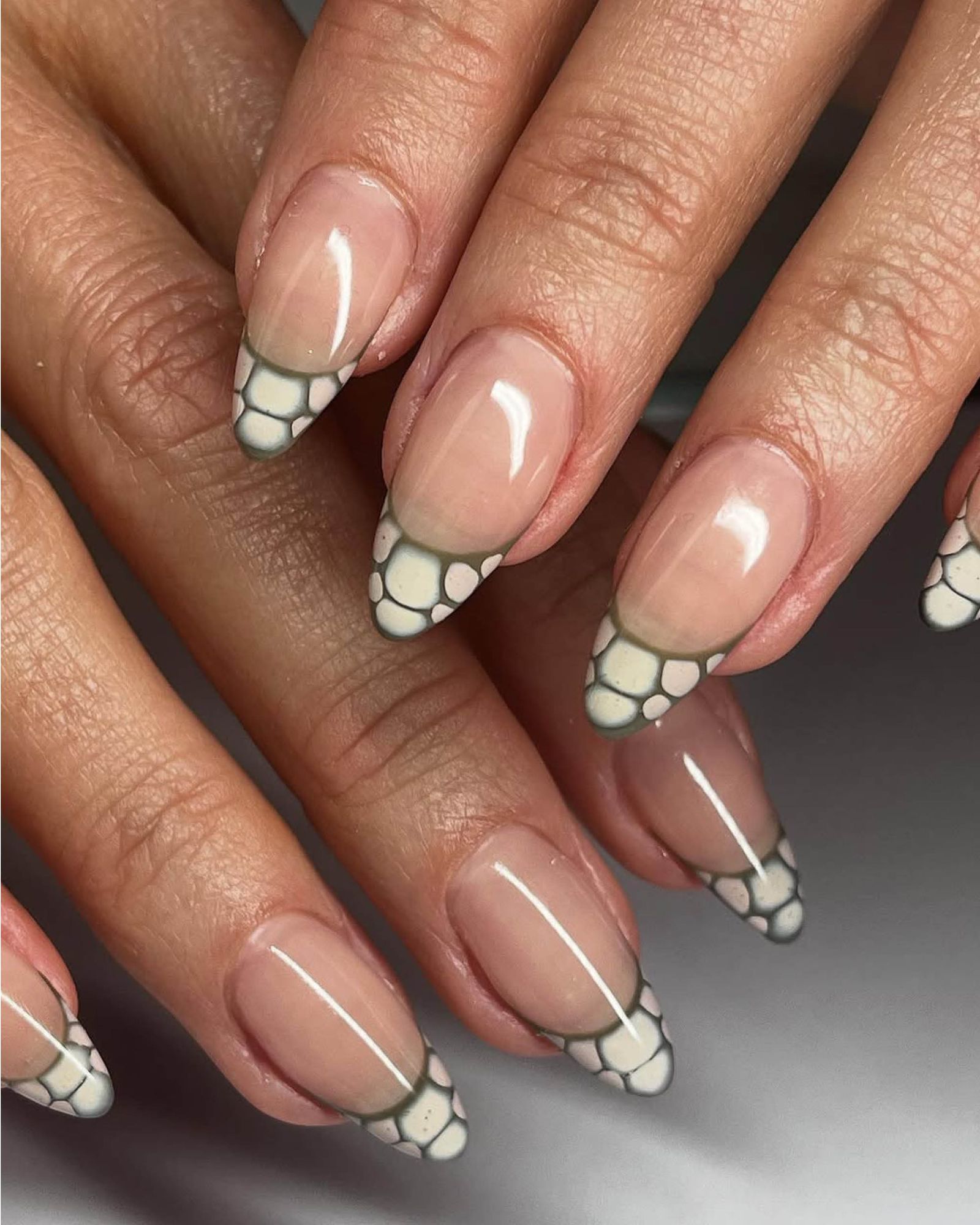 Layered hands showcase almondshaped nude nails with gray and cream snake skin French tips.